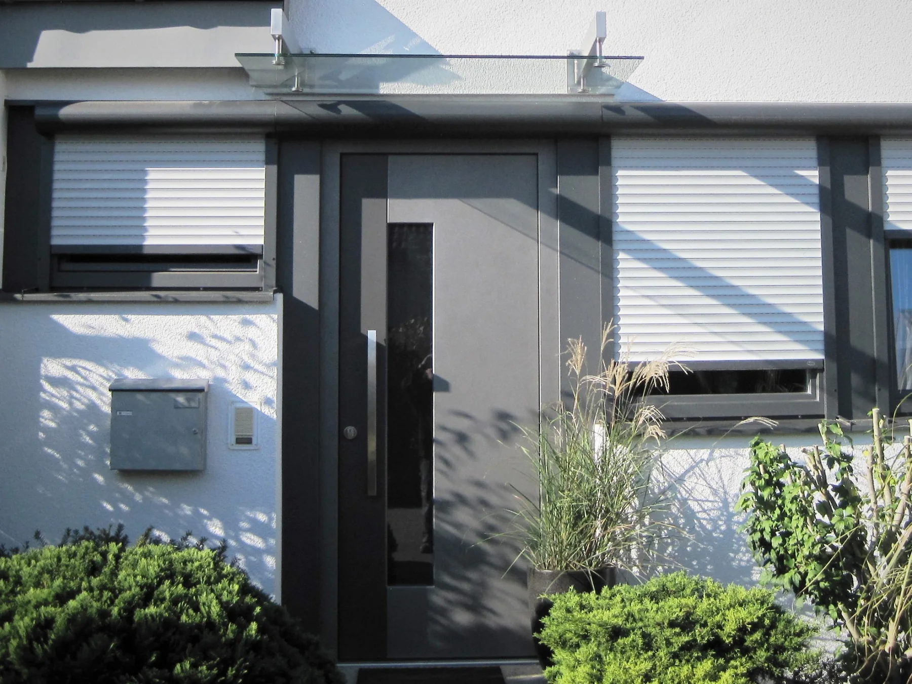 Graue moderne Haustür mit weißen Rollläden an einem sanierten Wohnhaus