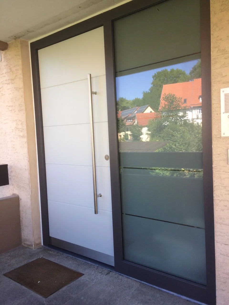 Moderne weiße Haustür mit langem Edelstahlgriff und verglastem Seitenteil